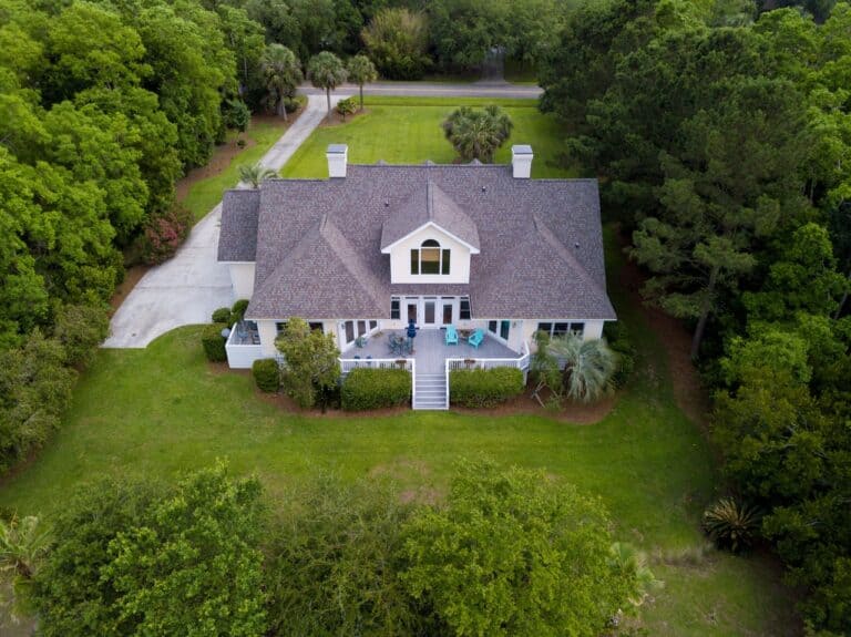 Aerial view of large home with new roof on wooded grassy property