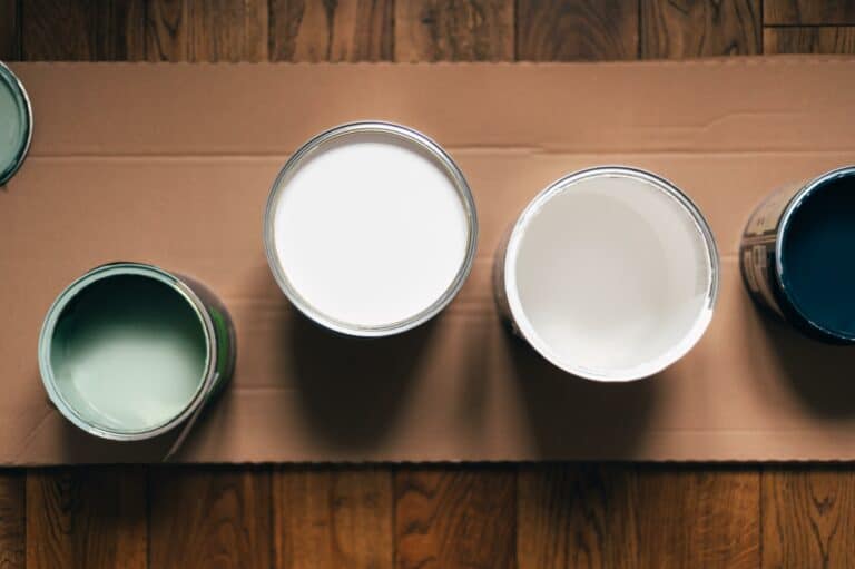 Paint cans during house renovation, process of choosing paint for the walls, different colors of white, green and blue on wooden floor