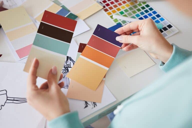 Close-up of unrecognizable female dressmaker sitting at table and viewing color swatches while choosing color for dress