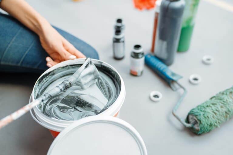 Female house painter mixes black and green paints in pail, closeup. Home repair, laughing woman doing appartment renovation, room decoration renovating
