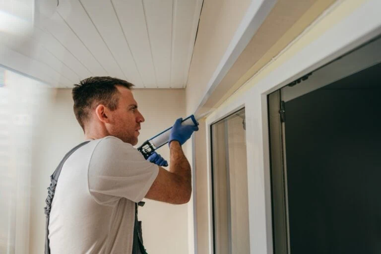 man caulking exterior of home in preparation for coating.
