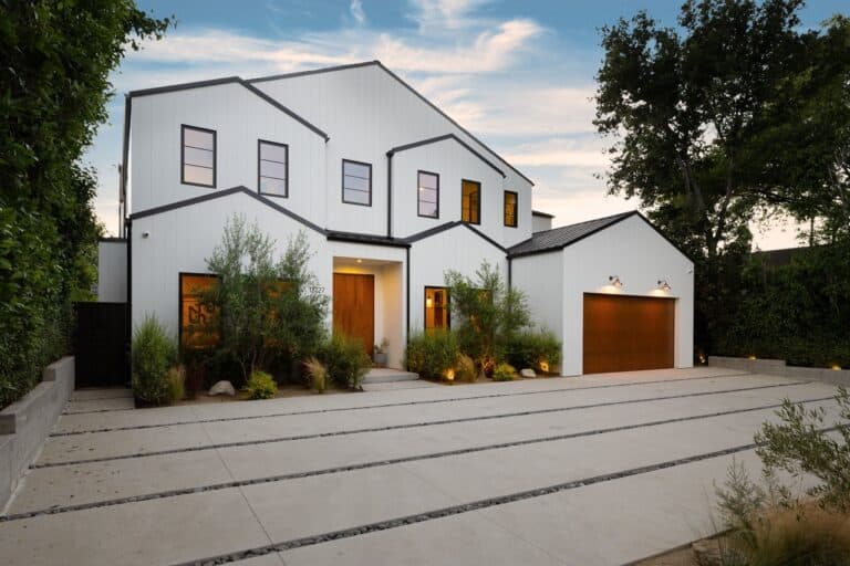 Modern white house exterior with wooden accents, surrounded by greenery, under a blue sky.