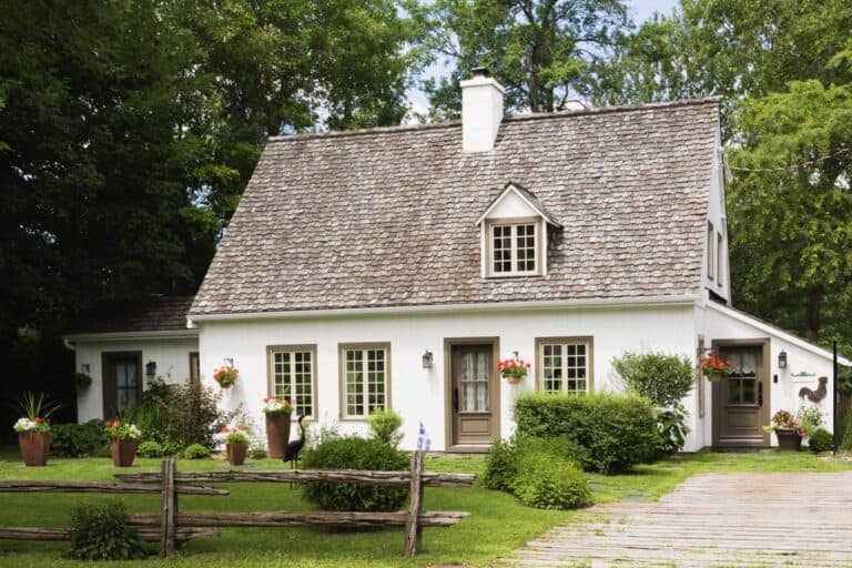 Old (circa 1886) white with beige and brown trim Canadiana cottage style home facade in summer, Quebec, Canada