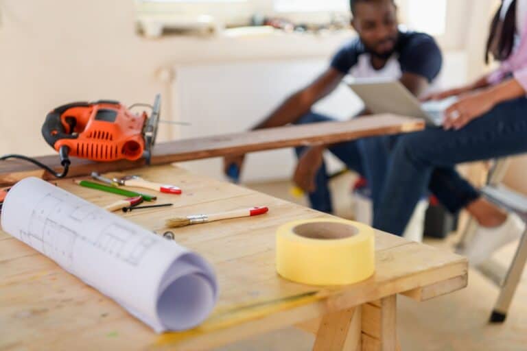 selective focus of wooden table with blueprint and couple sitting behind during renovation at home