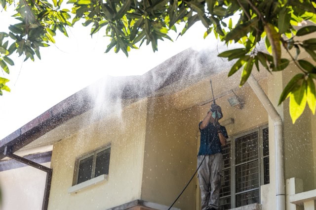 Worker using high pressure water jet spray gun to wash and clean dirt from roof ceiling at residential building